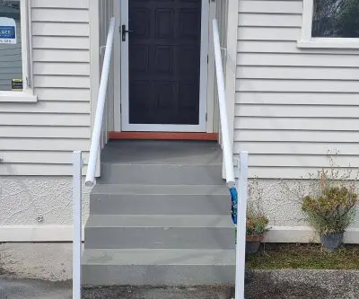 White post-mounted handrails on both sides of concrete steps up to a front door